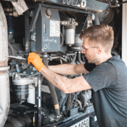 Mechaniker mit orangen Handschuhen arbeitet am offenen Motorraum eines Busses