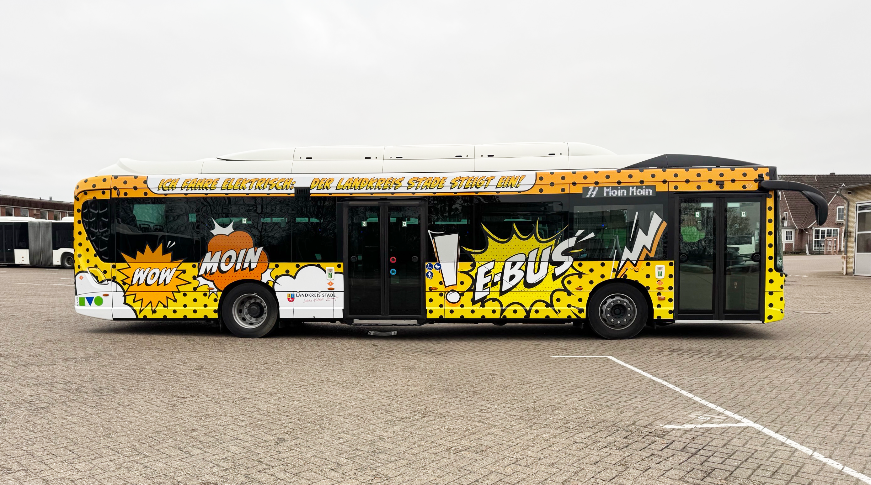 Stadtbus mit auffälligem gelb-schwarzem Design „Moin E-Bus“, seitlich fotografiert.